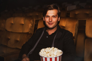 Handsome foreign men watch movies in modern theaters, holding popcorn to snack on during a fun movie to enhance the entertainment : man looked at the camera with pleasure in the cinema.