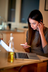 A young beautiful girl with a drink sitting at the table in an apartment and texting. Leisure, date, meeting