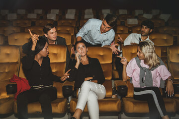 Young woman talking on the phone among moviegoers so annoying others that men and others who sit...