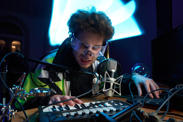Angry caucasian composer looks at camera and plays music using midi keyboard in dark room with...
