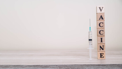 Word text VACCINE made of wooden cubes and syringe isolated on a wooden table background with copy...