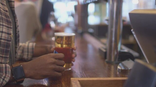 Close up of male customer in bar paying bartender for drink using contactless card and social distancing during health pandemic - shot in slow motion