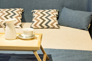 wooden tea table stands on the bed with cups. Bed with pillows and blue duvet and wooden chest of drawers