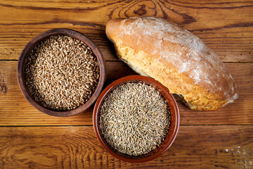rye and wheat grains in ceramic bowls and bread on wooden table, selective focus..
