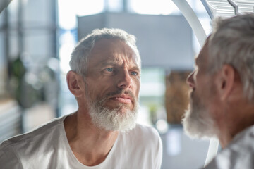 Bearded grey-haired man looking at the mirror