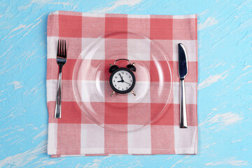 Concept of intermittent fasting, diet and weight loss. Plate as Alarm clock on blue background
