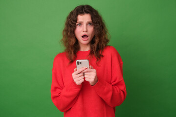 Beautiful young girl in red clothes on a green background. Upset girl with a phone in her hands