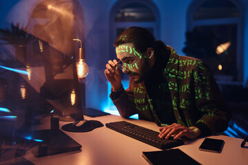 Working late computer specialist which does his job using desk computer in dark office room.