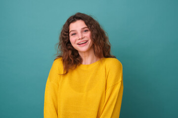 A cheerful young woman with a pleasant radiant contented expression, dressed in a casual yellow jumper isolated on a blue background.