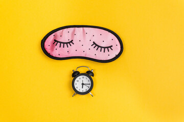 Sleep concept showing an eye mask and an alarm clock on a yellow background. copy space