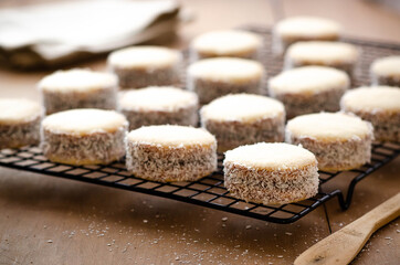 Cornstarch alfajores with milk caramel and coconut on a black rack, a beige napkin and wooden knife. 