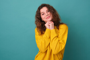The girl looks sweetly into the camera holding her hands near her head in yellow clothes on a blue background