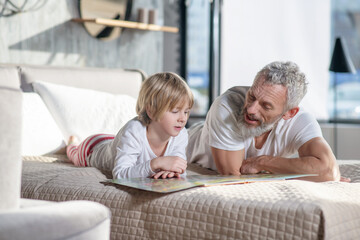Obraz premium Gray-haired man reading children book and child
