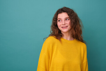 Fototapeta premium Horizontal shot of a cute young curly girl, has a good mood, feels nice to receive a compliment, focused away, isolated on a blue background