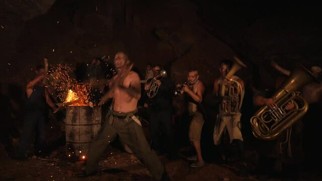 Crazy orchestra playing. Funny musicians play underground in a cave at night. Crazy people play musical instruments and dance funny dances in the cave. Funny bass guitarist, tubist, trumpeter, drummer