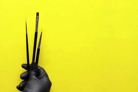 brushes for coating gel varnish in hand with a black glove and on a bright modern yellow background - Powered by Adobe