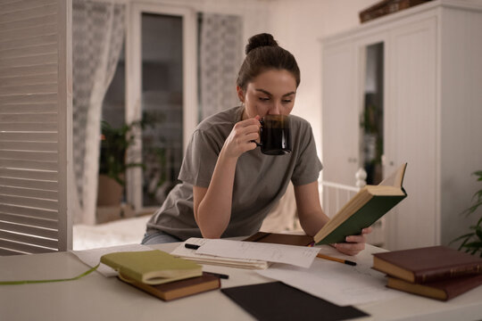 Student reading book and drinking coffee during exam preparation