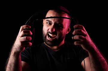 Angry screaming bearded arabic musician dj tearing headphones on black isolated background....