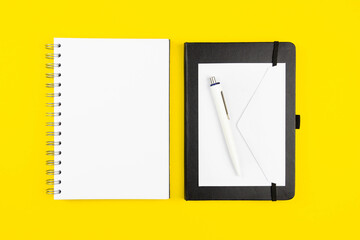 Office desk table with blank paper notebook mockup and pen. Yellow background, copy space. Top view flat lay.