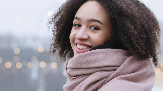 Portrait of african american young girl dark-skinned lady with curly afro hairstyle wears pink warm scarf in winter cold weather stands alone outdoors exhaling steam smiling toothy looking at camera