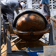 Construction workers pouring cement, sandstone and water into the mortar mixer.