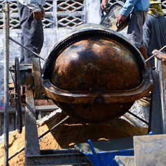 Construction workers pouring cement, sandstone and water into the mortar mixer.