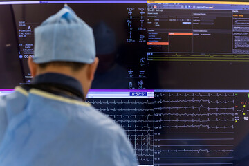 an angiologist sits in front of a screen showing a patient's heartbeat