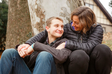 A loving mom and son lean together against large sycamore tree outside