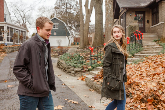 A brother and sister walk together down suburban sidewalk in autumn