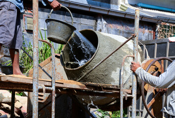 Construction workers pouring cement, sandstone and water into the mortar mixer.