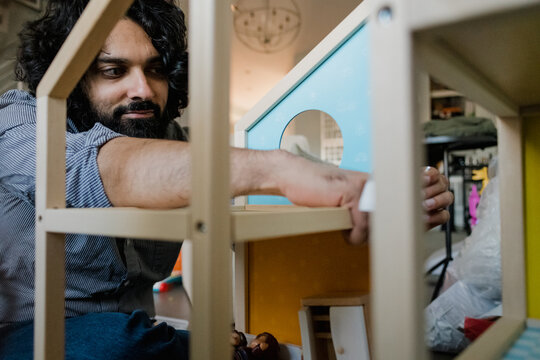 Adult man assembling dollhouse in domestic living room