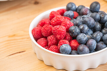 mixed fresh fruits (strawberry, raspberry, blueberry, kiwi, mango) on wood bowl