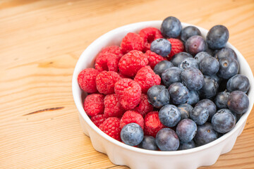 mixed fresh fruits (strawberry, raspberry, blueberry, kiwi, mango) on wood bowl