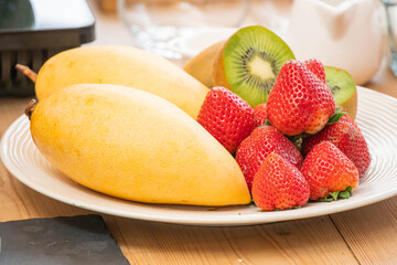 mixed fresh fruits (strawberry, raspberry, blueberry, kiwi, mango) on wood bowl