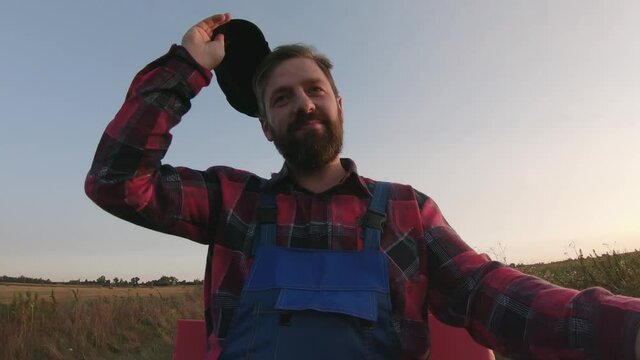 View from the steering wheel of happy middle-aged farmer with beard on shaking minitractor, driving through the countryside from the market after selling his own crop. Man waves his cap affably