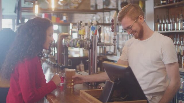 Female customer in bar paying bartender for drink using contactless card and social distancing during health pandemic - shot in slow motion