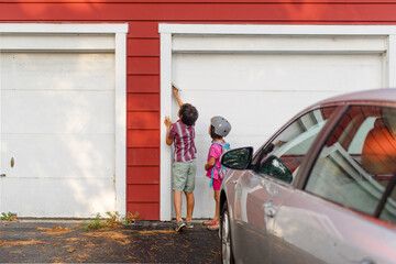 Two small children stand together and press keypad to enter garage
