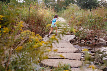A small child runs along stone pathway through a prairie over a creek