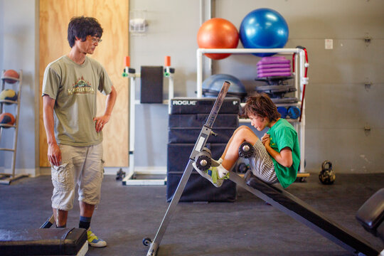 A boy does stomach crunches on gym equipment while father looks on