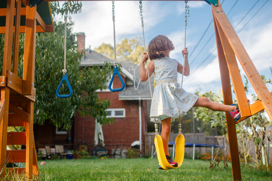 A little girl in fancy dress balances one-legged on a yellow swing