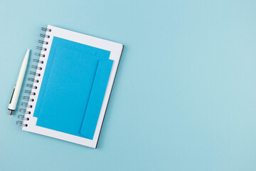Modern office workplace with paper notebook, pen and envelope on blue background. Top view. Copy space. Flat lay.