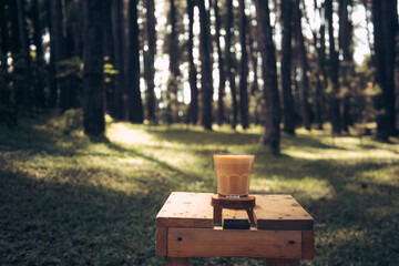 A cup of coffee on wooden table with outdoors green summer forest background 