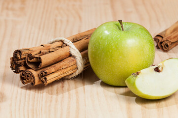 Green apple with a cinnamon stick; photo on wooden background.