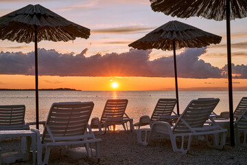Straw beach umbrellas and chairs on a sunset beach with beautiful clouds