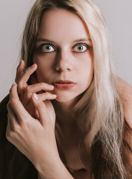 Portrait of beautiful nude young woman with long blond hair covering her breast while lying on bed