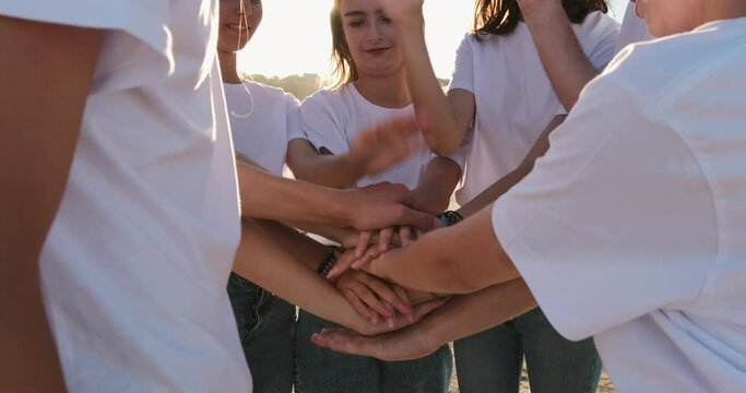 A group of seven young men in white T-shirts fold their arms in the center in front of them. Guys and girls bring team spirit together.