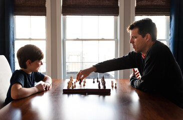 Father and son sitting at a table indoors playing a game of chess.