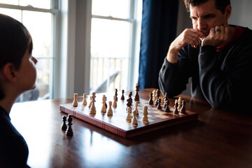 Father and son sitting at a table indoors playing a game of chess.