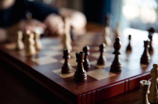 Close up of pieces in a chess game with child blurred in background.