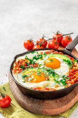 Shakshouka with avocado in a frying pan on a gray table close-up. Shakshouka of tomato sauce, eggs, spices, onions, garlic, and avocado. Tasty Maghreb style breakfast. Copy space for text.